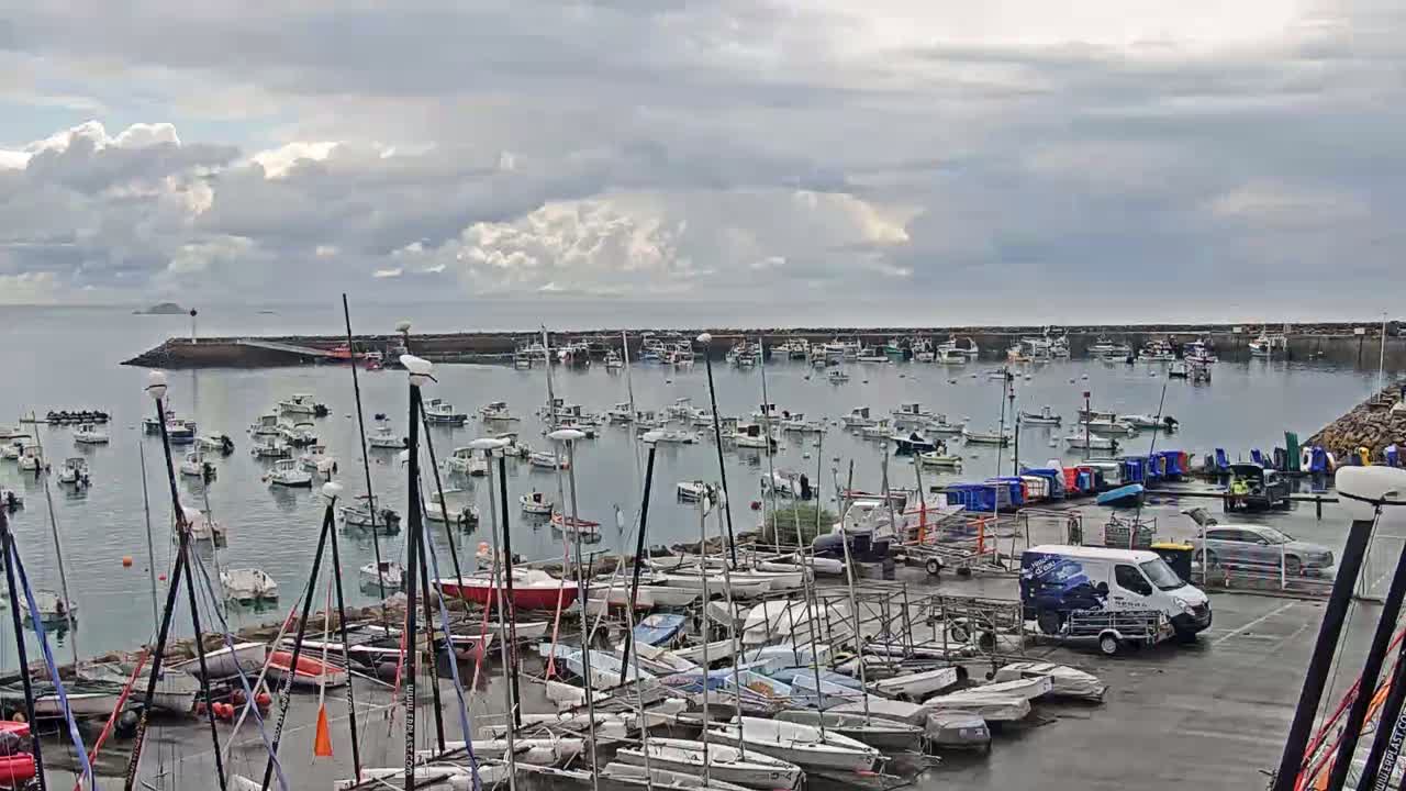 Many sailboats and motorboats are moored in a harbor under a cloudy sky.