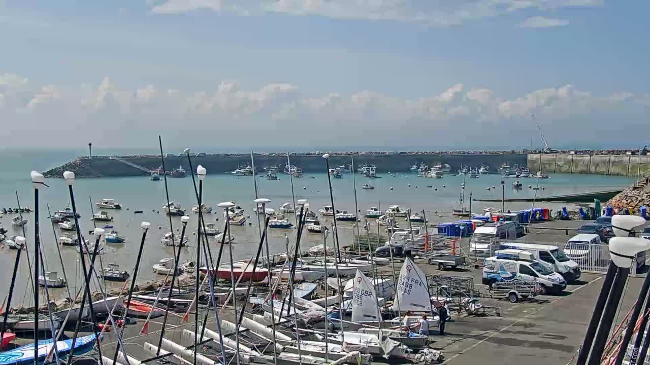 A harbor filled with numerous sailboats and motorboats is partially exposed at low tide under a partly cloudy sky.