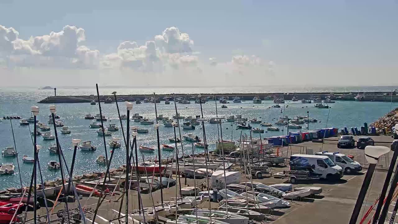 A harbor filled with numerous sailboats and motorboats under a partly cloudy sky.