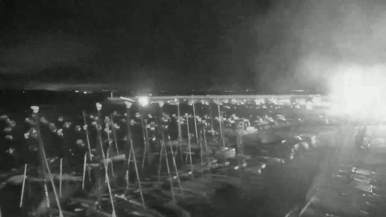 A nighttime, low-light view shows numerous upright poles with indistinct objects attached at the top, possibly in a parking lot or field.