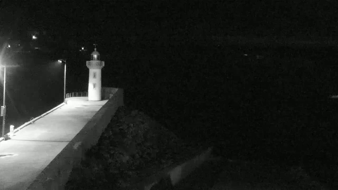 A lighthouse stands at the end of a pier at night, illuminated by several lights.