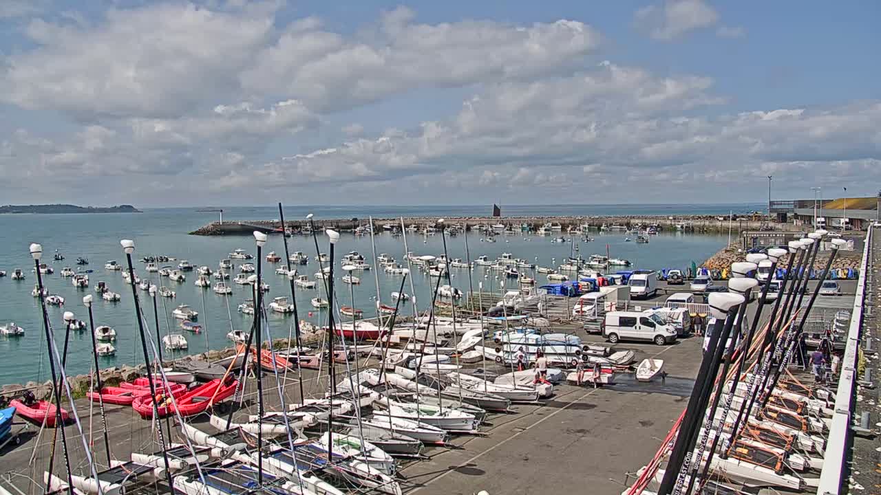Many sailboats and motorboats are docked in a harbor on a partly cloudy day.