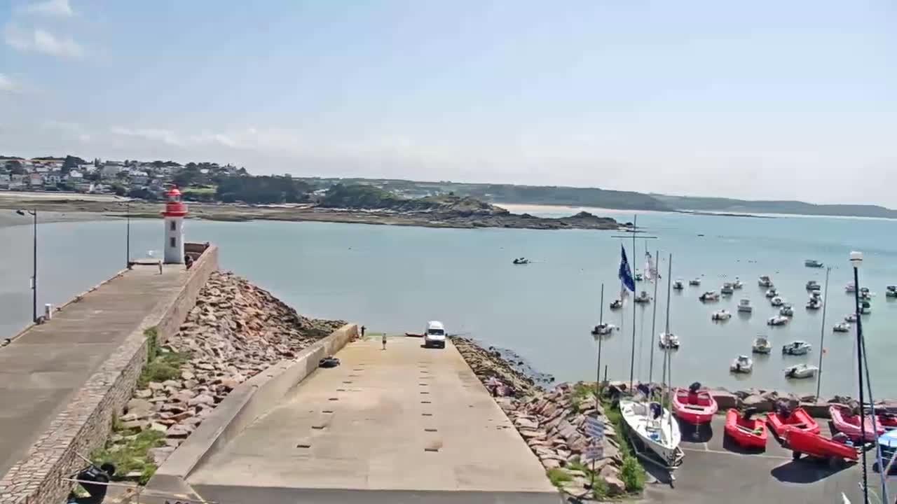 A harbor with a lighthouse and numerous small boats is shown on a sunny day.