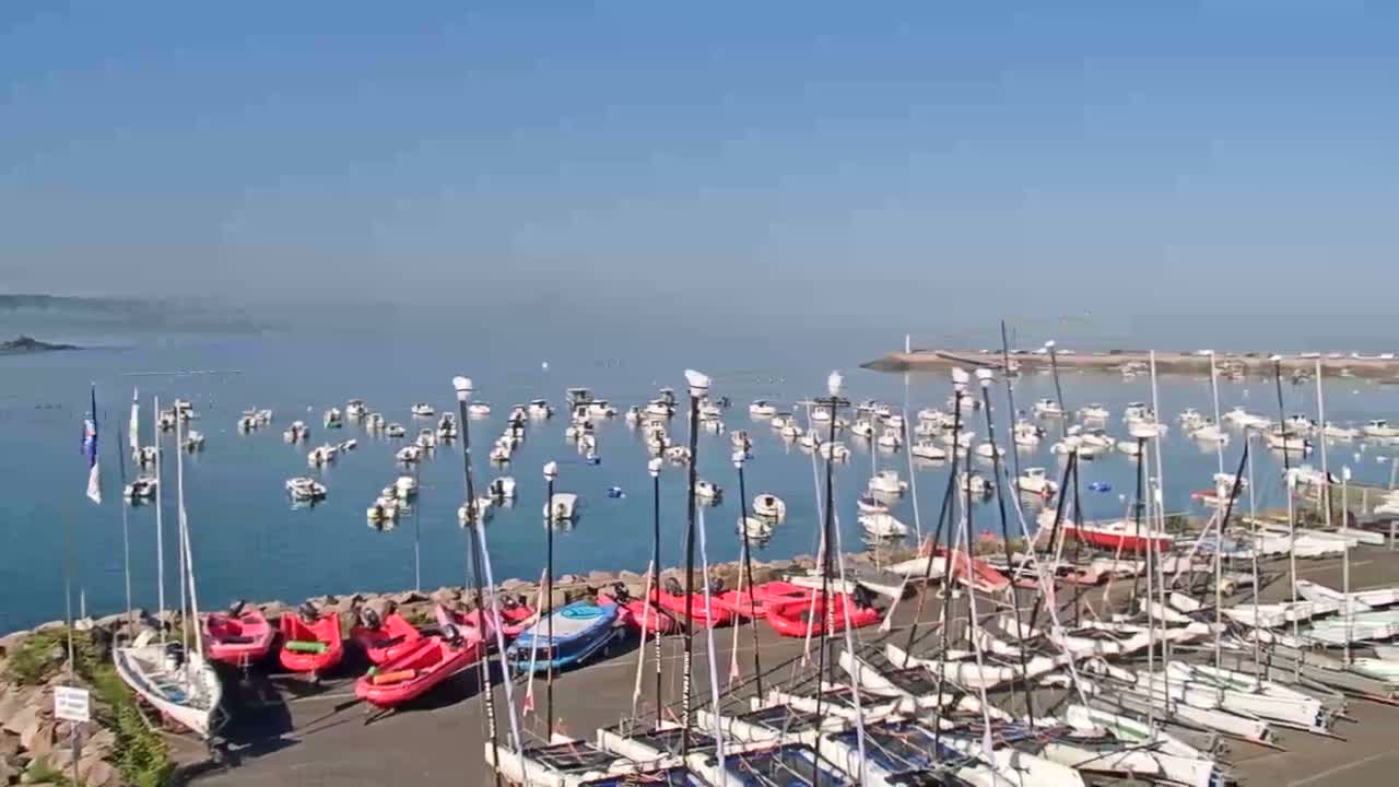 Many sailboats and small motorboats are docked in a harbor on a calm, sunny day.