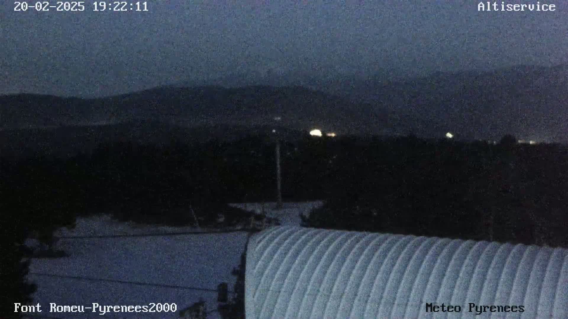 A nighttime view shows a snow-covered landscape with dark mountains in the background under a dark sky.