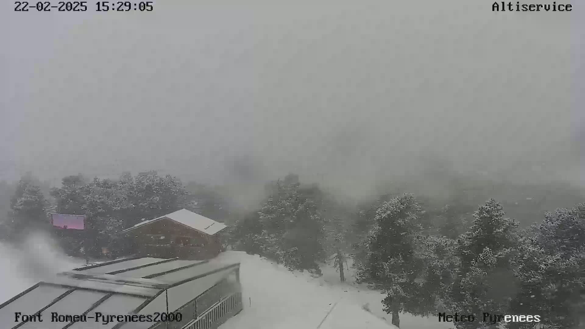 A snow-covered landscape with buildings and trees is seen through a heavy snowstorm.