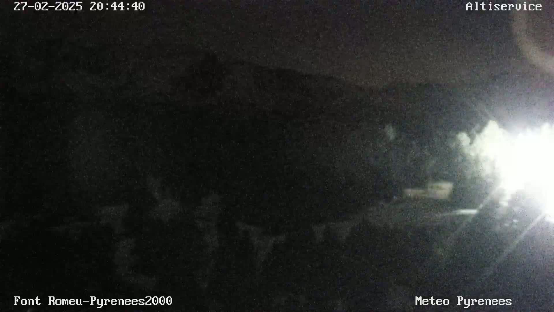 A nighttime, low-visibility view of dark mountains and a foreground of trees or bushes under a dark sky.