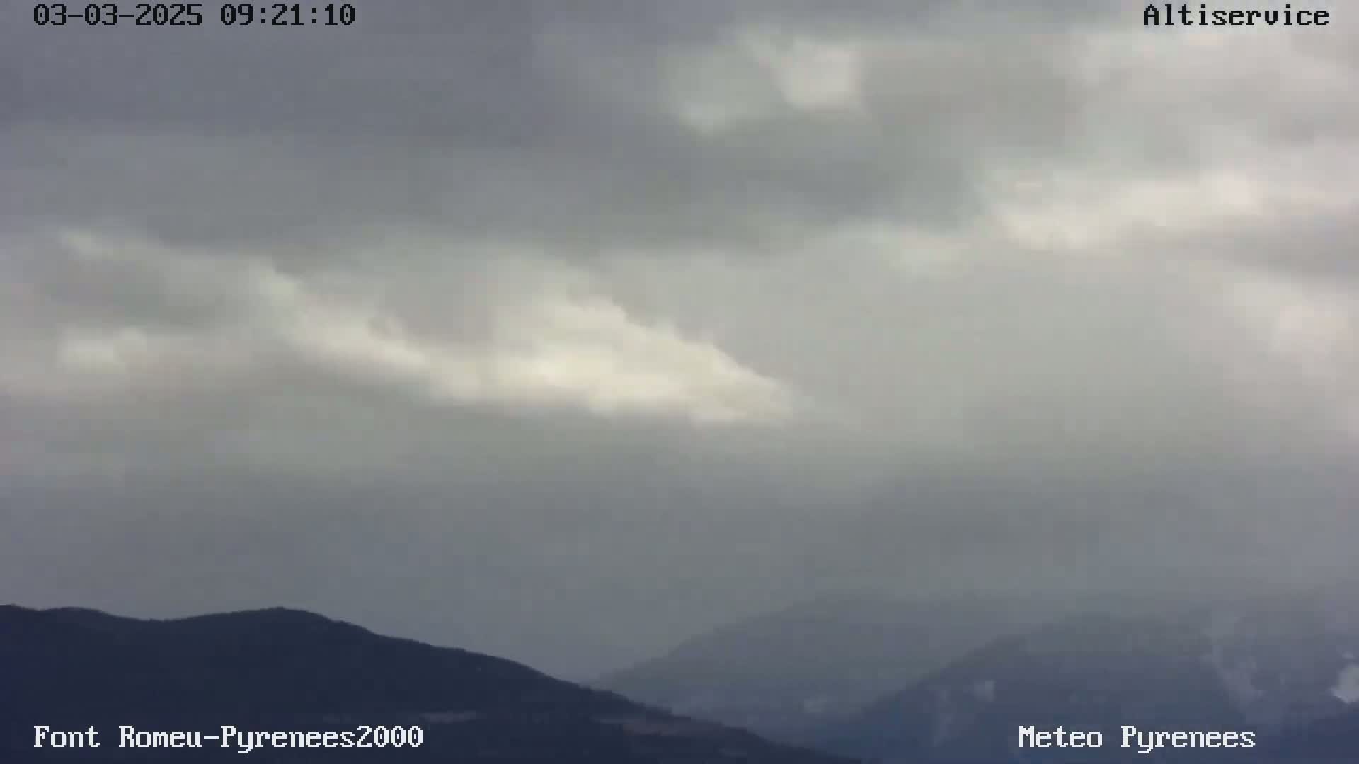 A view of overcast skies and distant mountains under a light rain.