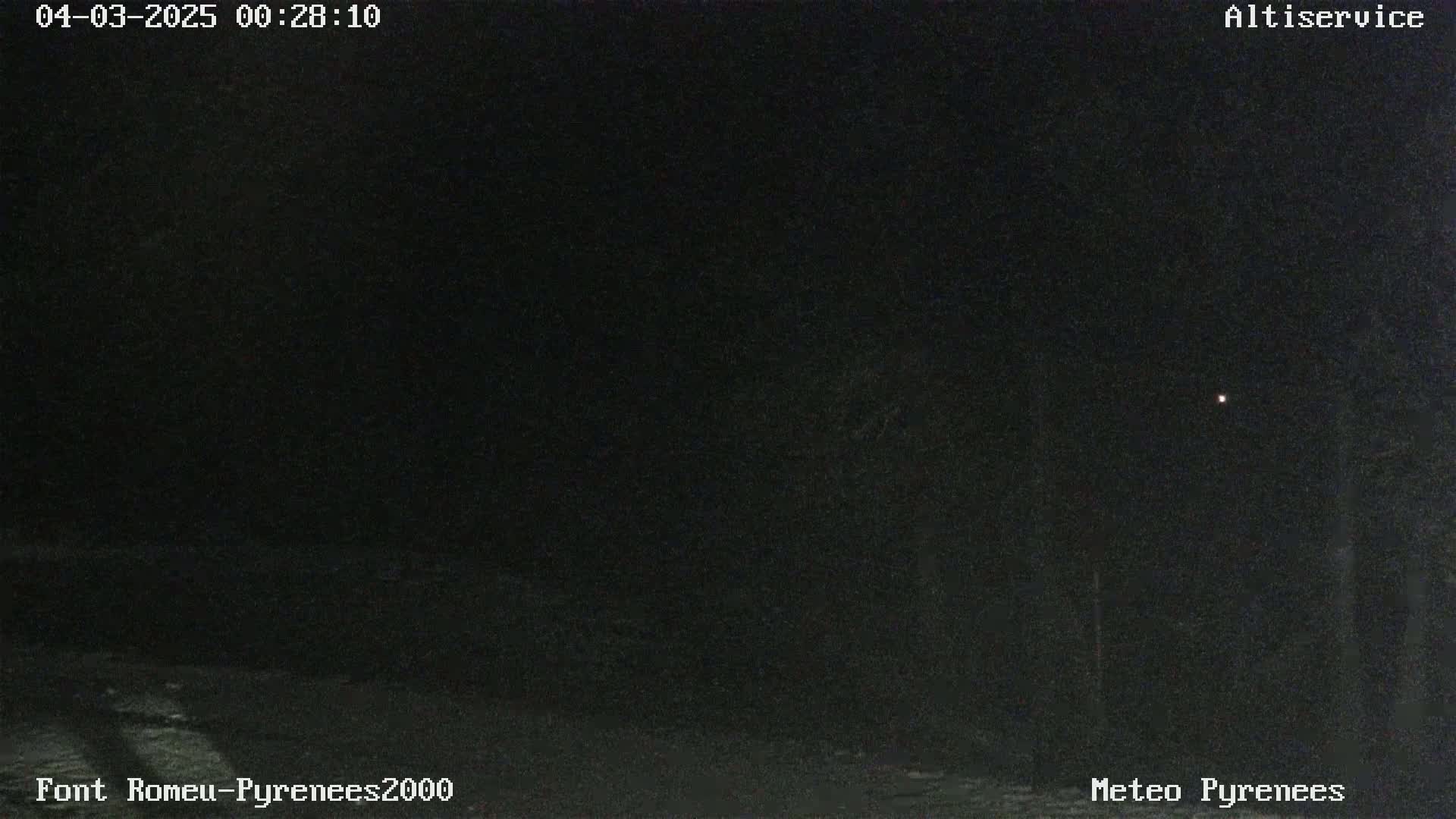 A dark, nighttime scene shows a dimly lit area with a single, faint light in the distance.