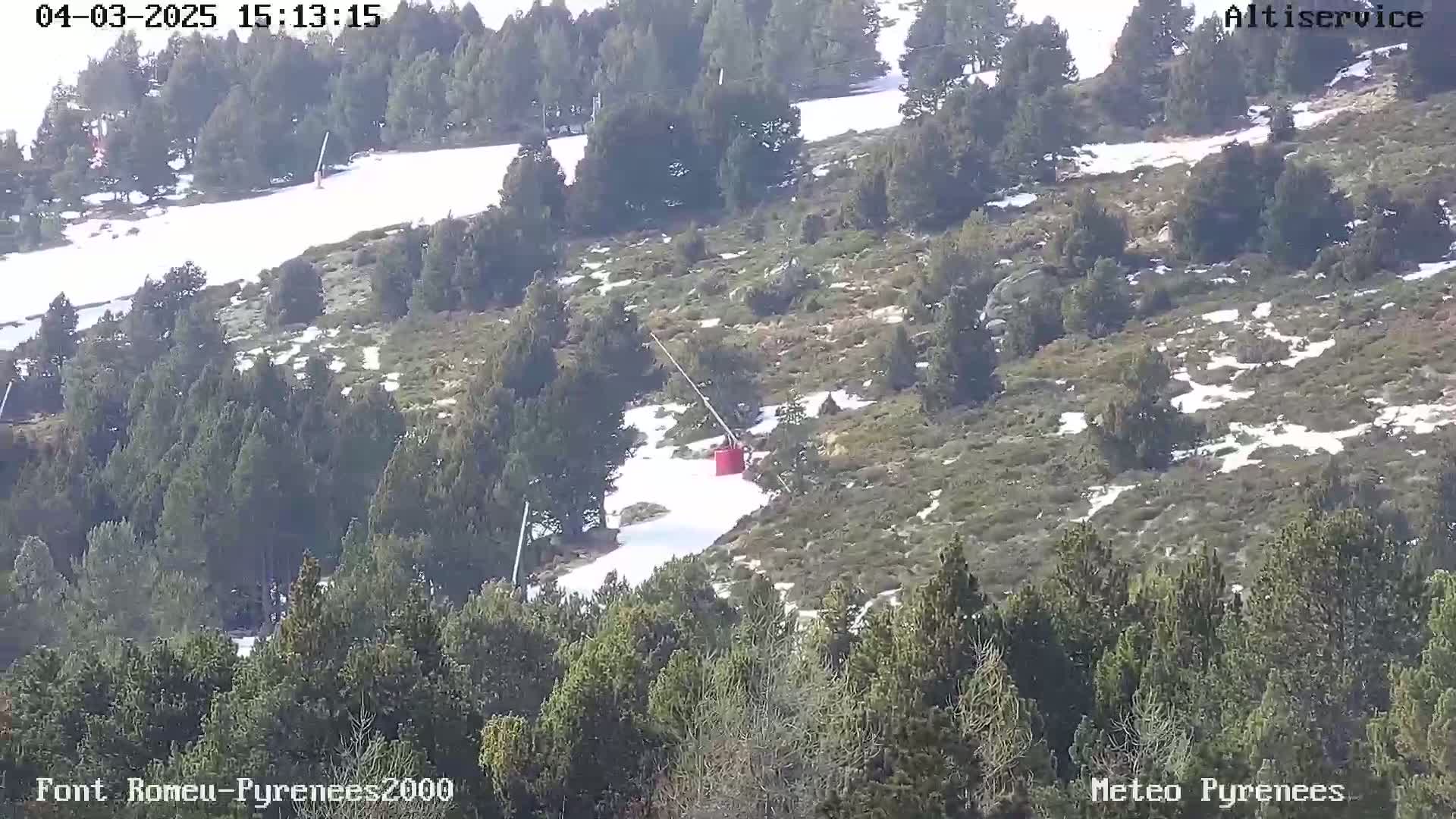 A red chairlift carriage is visible on a snowy hillside amongst evergreen trees on a partly sunny day.
