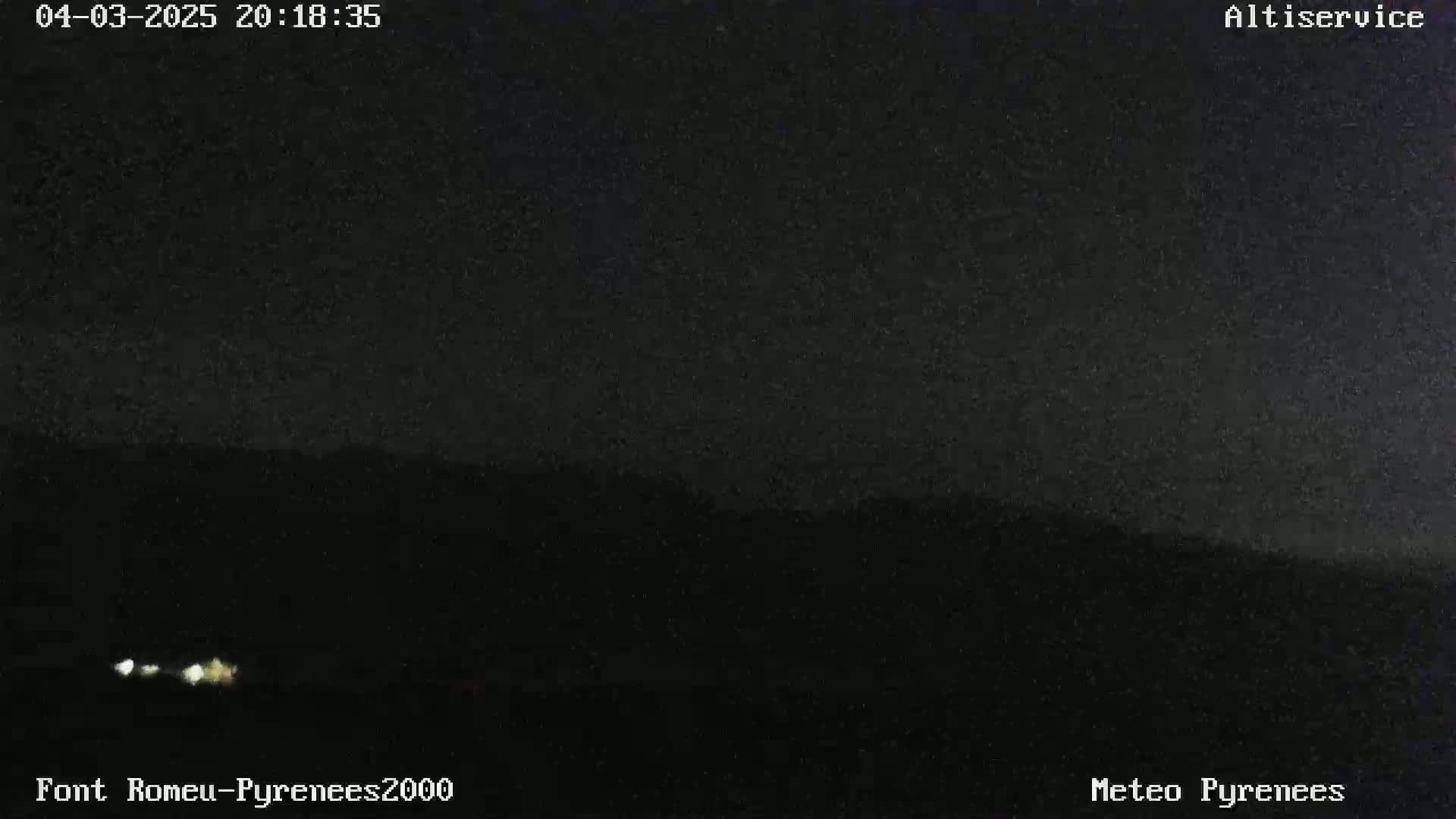 A nighttime long shot shows a dark landscape with faintly visible lights in the distance under a clear, dark sky.