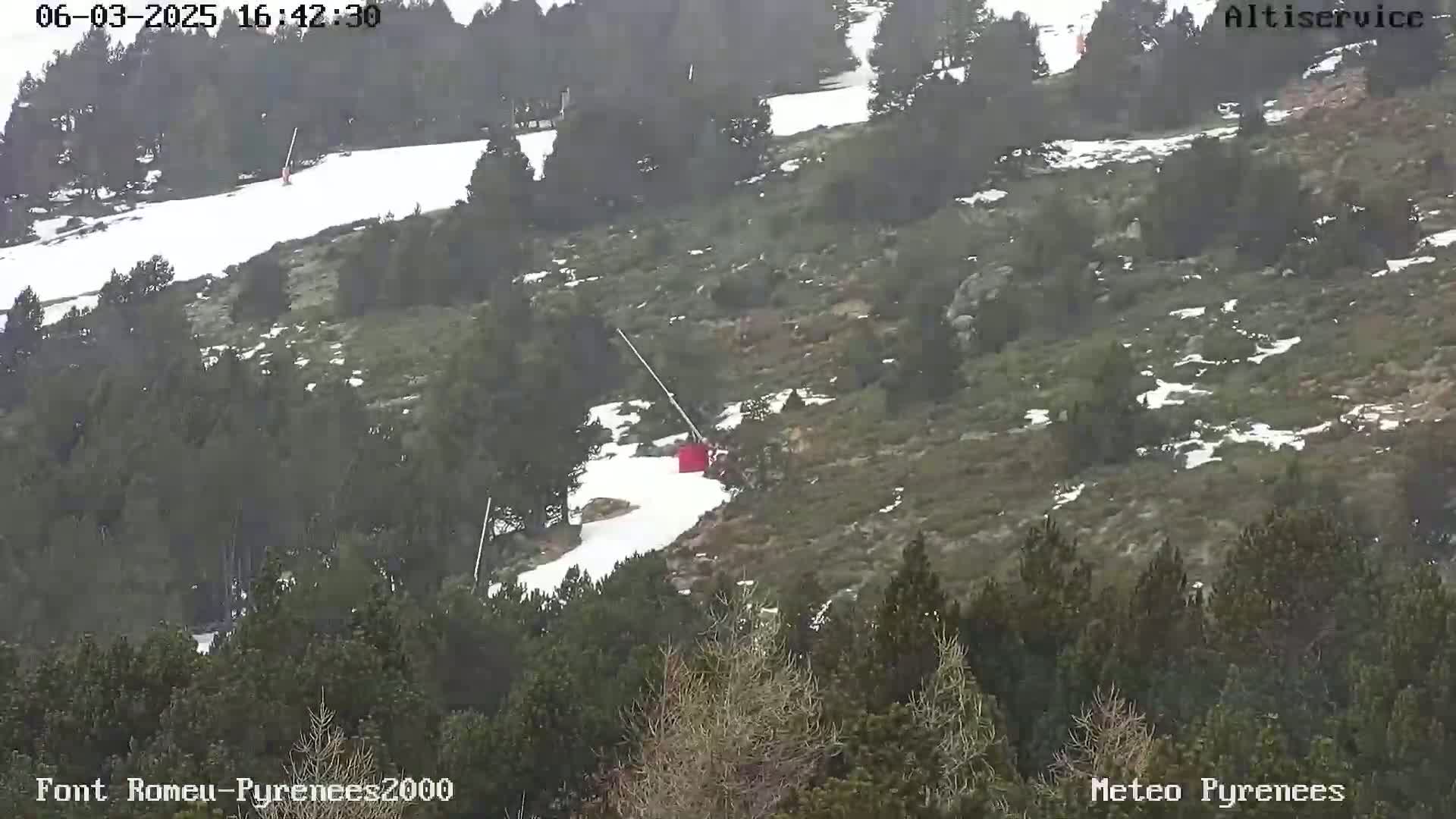 A chairlift ascends a snow-dusted hillside covered in dark green vegetation.