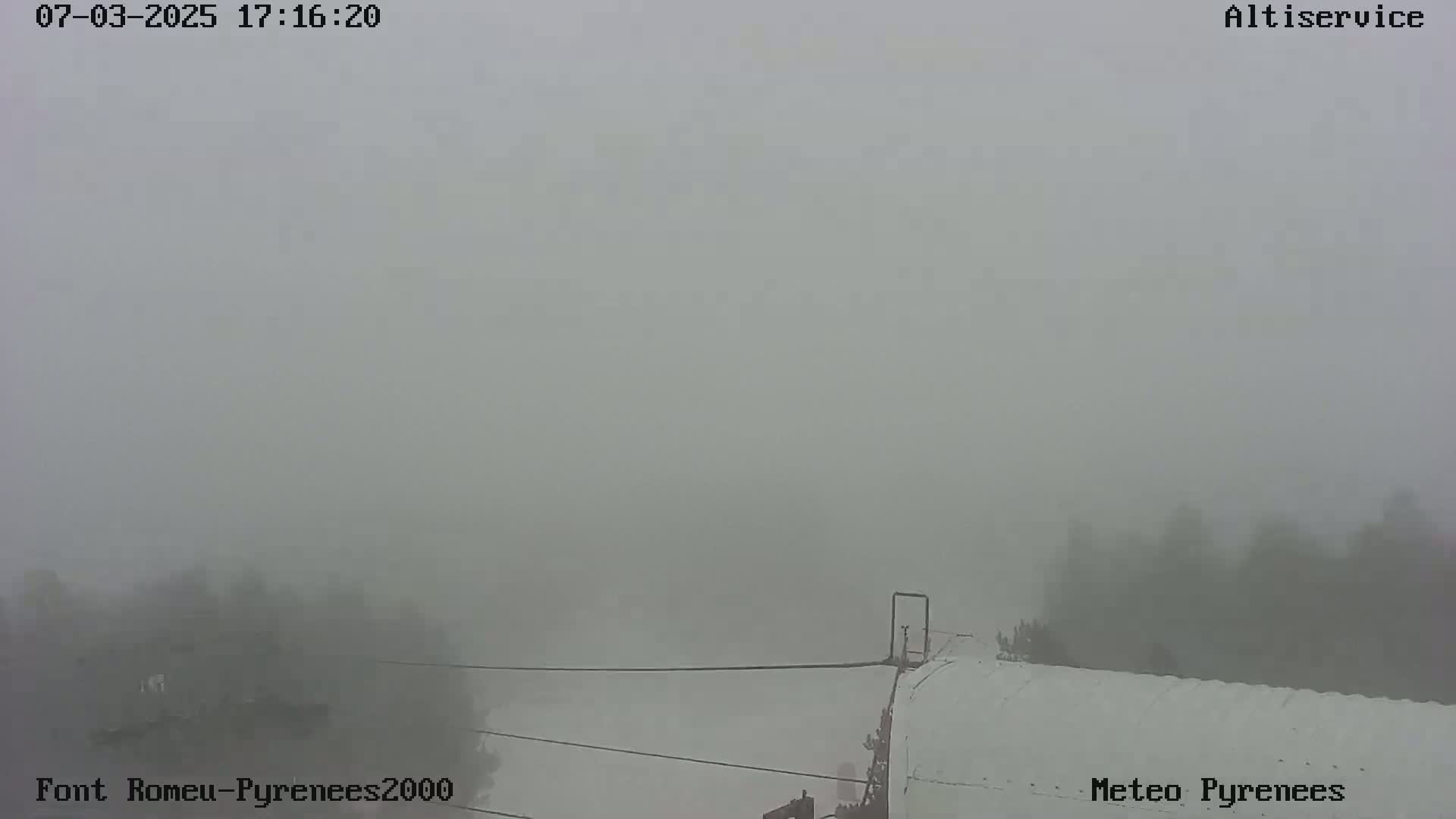 A thick fog obscures the view of a landscape with some trees and a portion of what appears to be a building or structure.