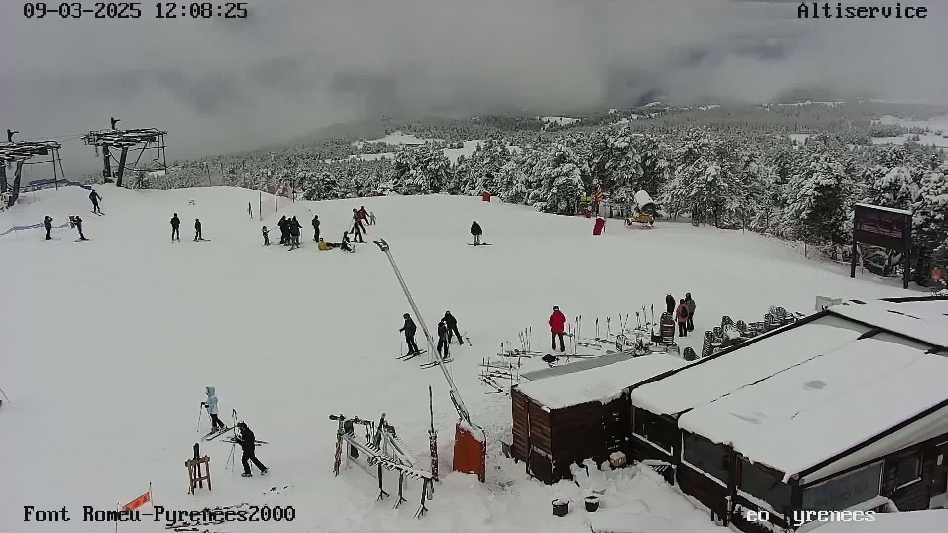 A snow-covered ski slope with several skiers and snowboarders, a ski lift, and a snow-covered building under an overcast sky.