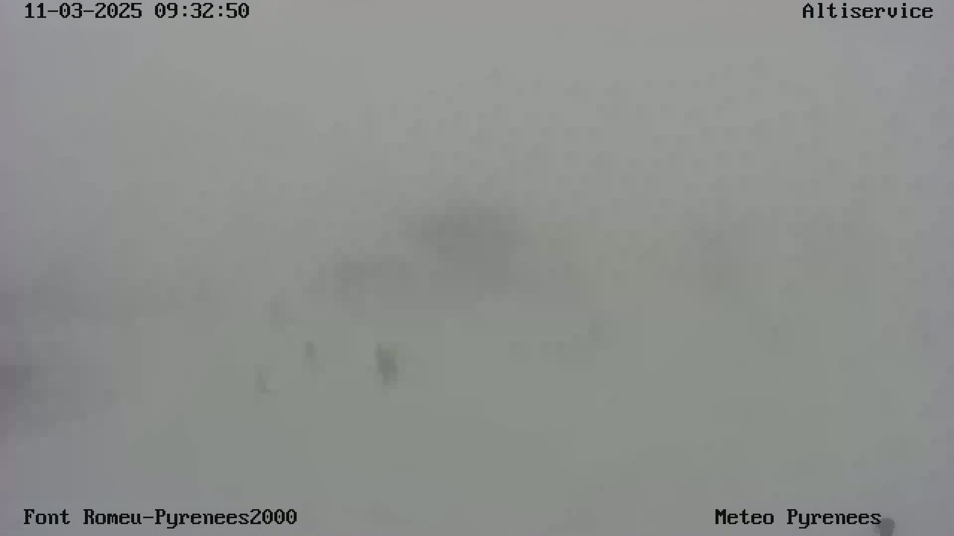 A very foggy or snowy outdoor scene shows a few indistinct shapes in the far distance.