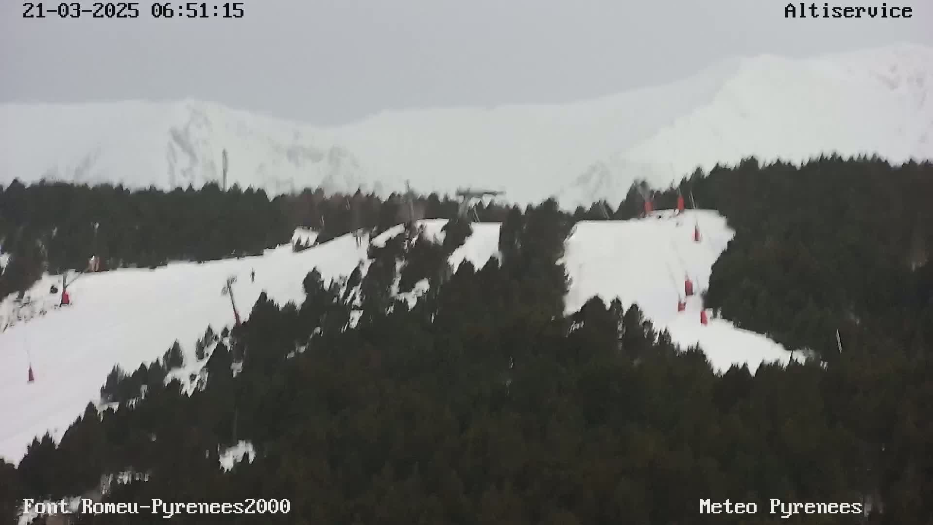A snow-covered ski slope with several skiers and ski lifts is visible, surrounded by dark evergreen trees under an overcast sky.
