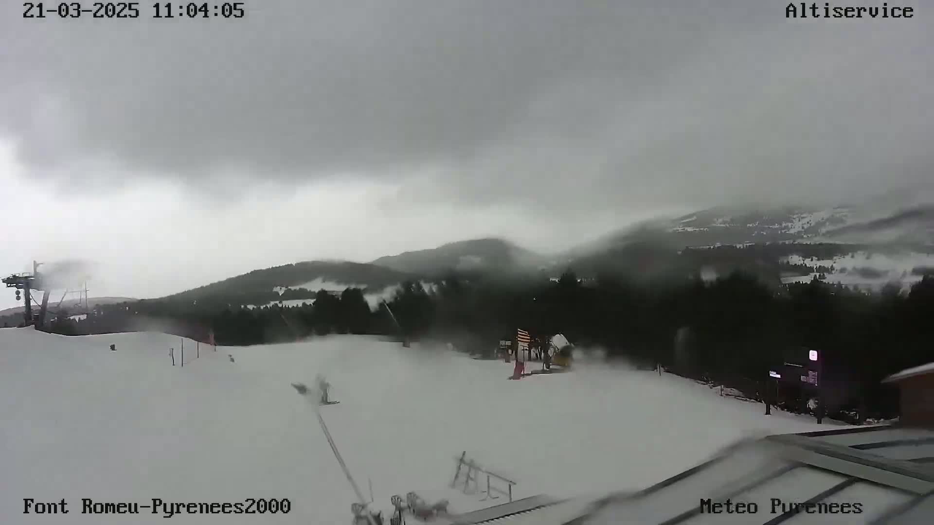 A snow-covered ski slope is visible under an overcast sky, with snow blowing across the landscape.
