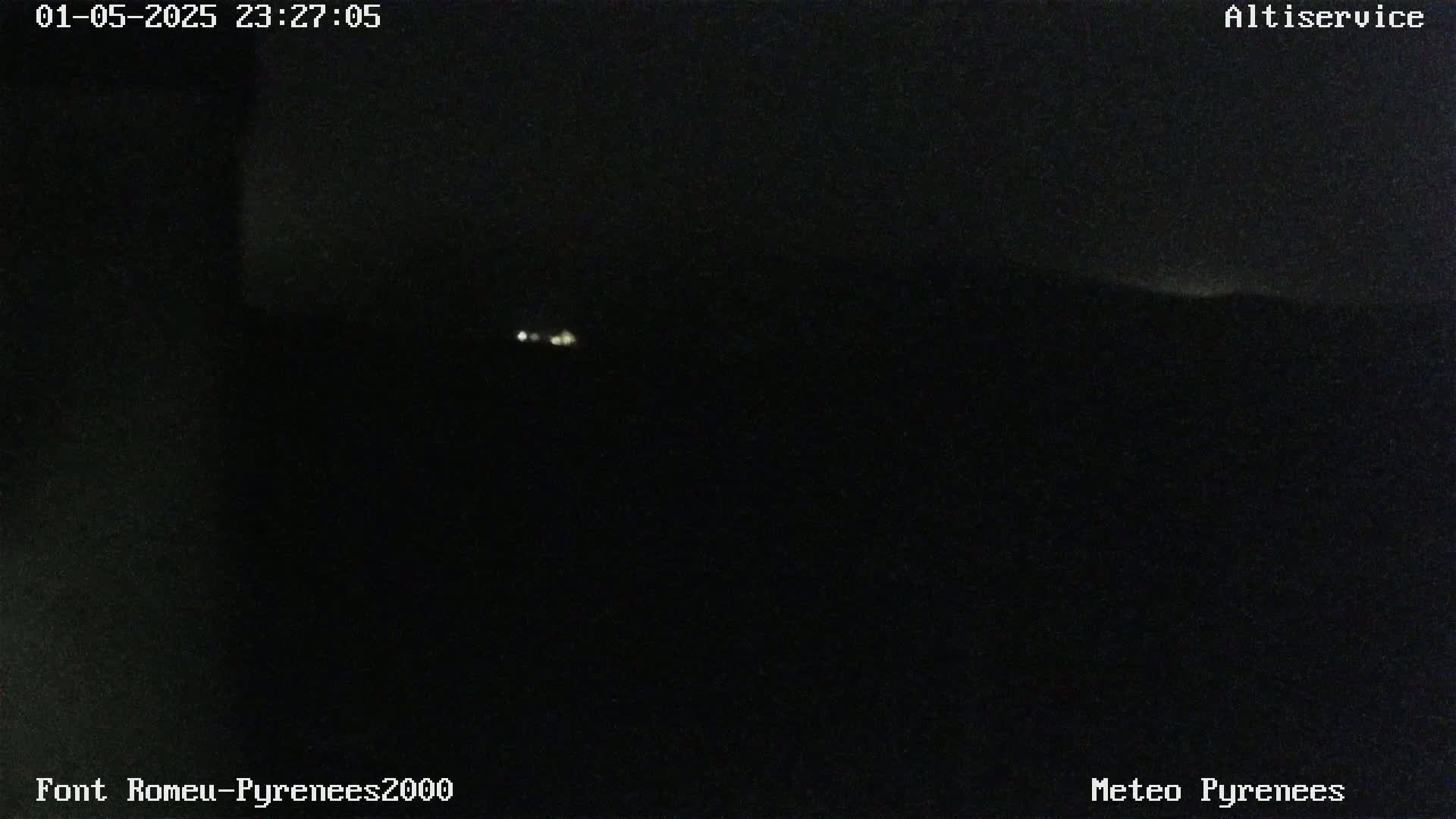 A nighttime, dark view shows faint lights in the distance under a clear, dark sky.