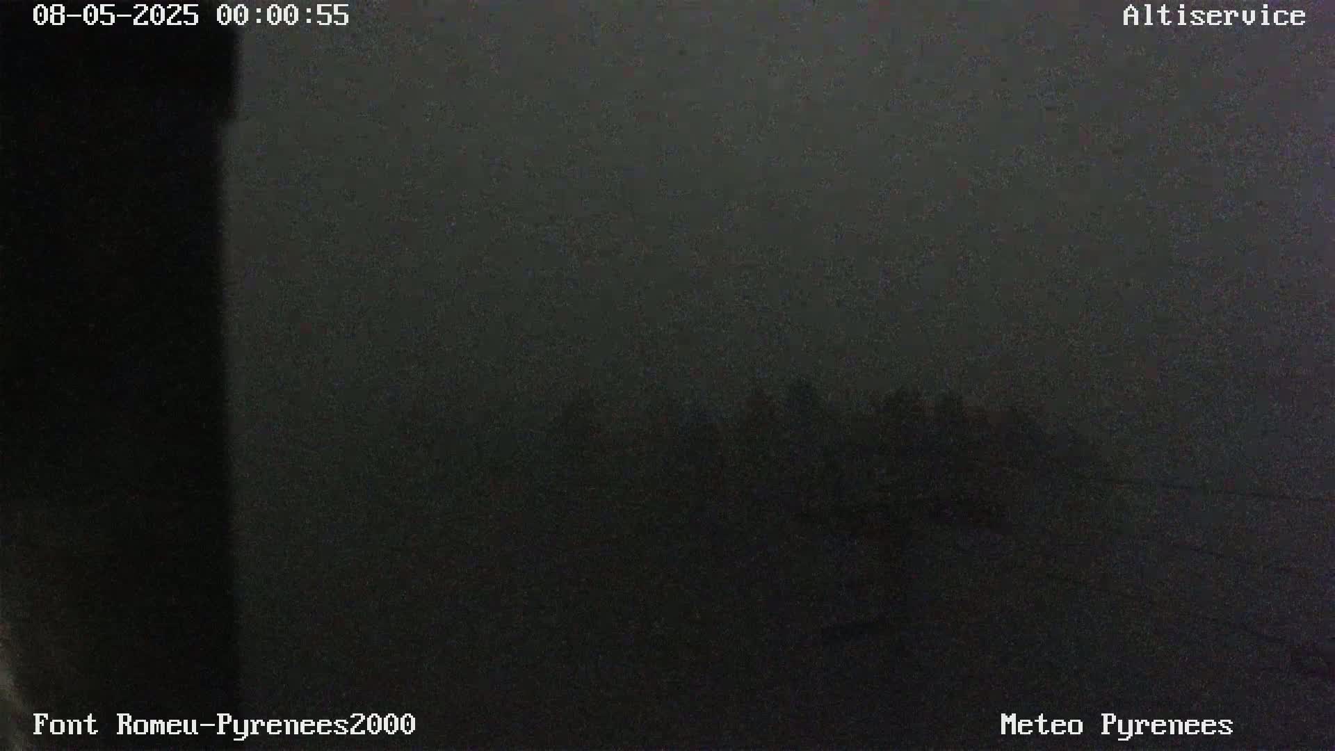 A dark, nighttime outdoor scene shows a hazy view of indistinct objects in the distance under a foggy sky.