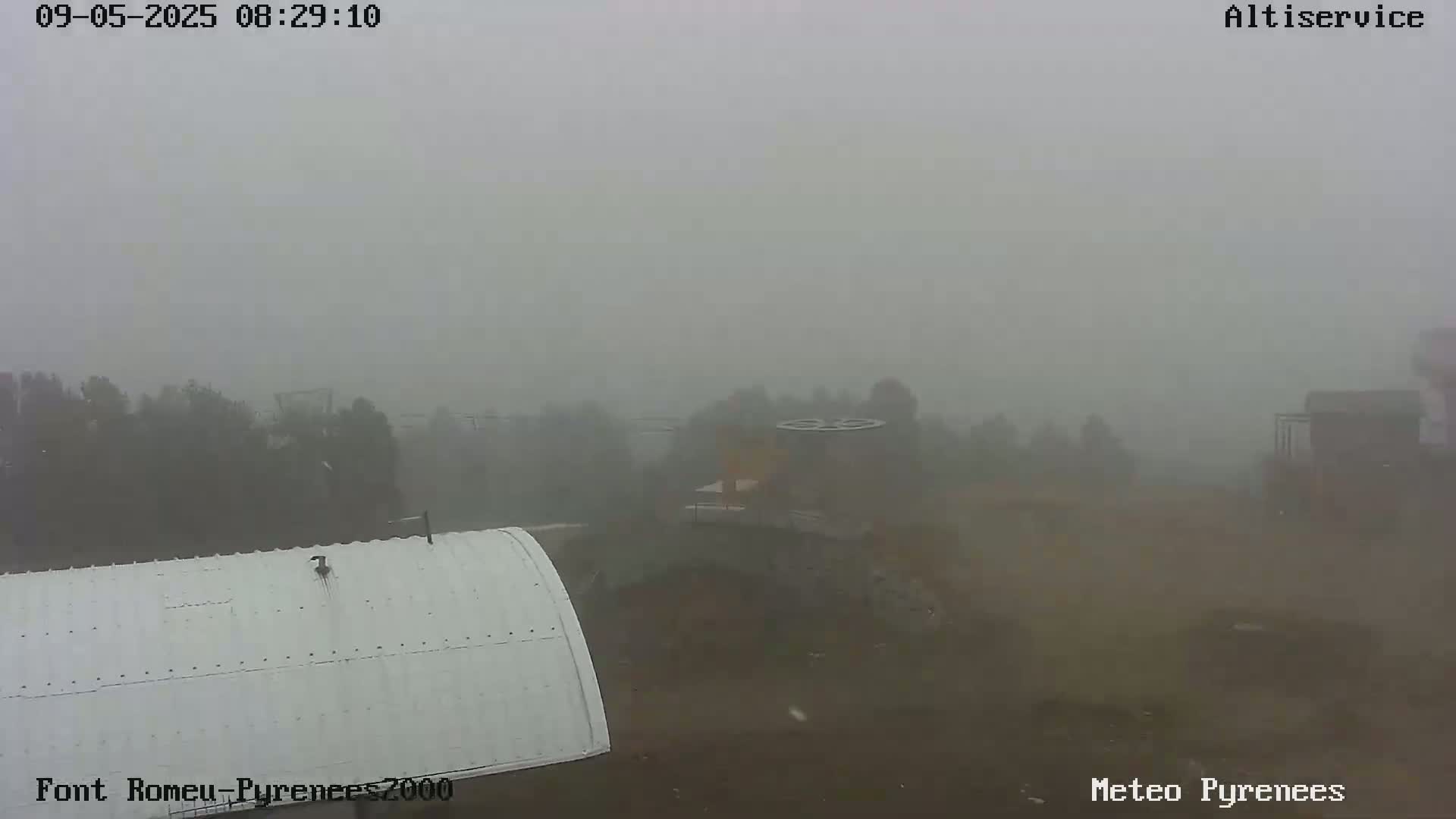 A thick fog obscures the view of a landscape containing trees, buildings, and a white curved structure, in what appears to be an outdoor setting.