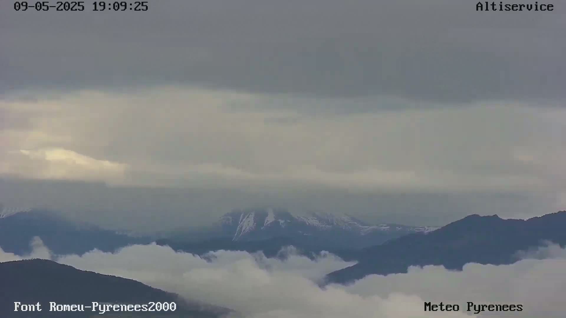 Snow-capped mountains are partially obscured by a low layer of clouds under an overcast sky.