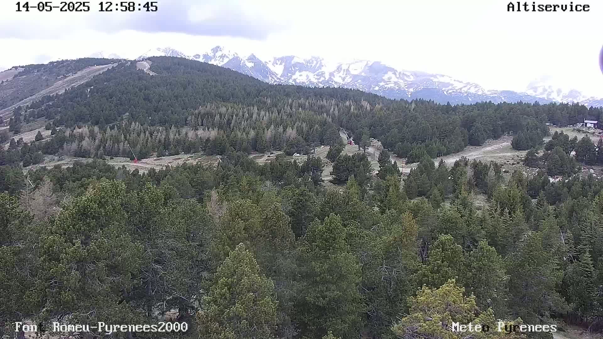 A mostly cloudy day reveals a mountainous landscape of evergreen forests with snow-capped peaks in the distance.