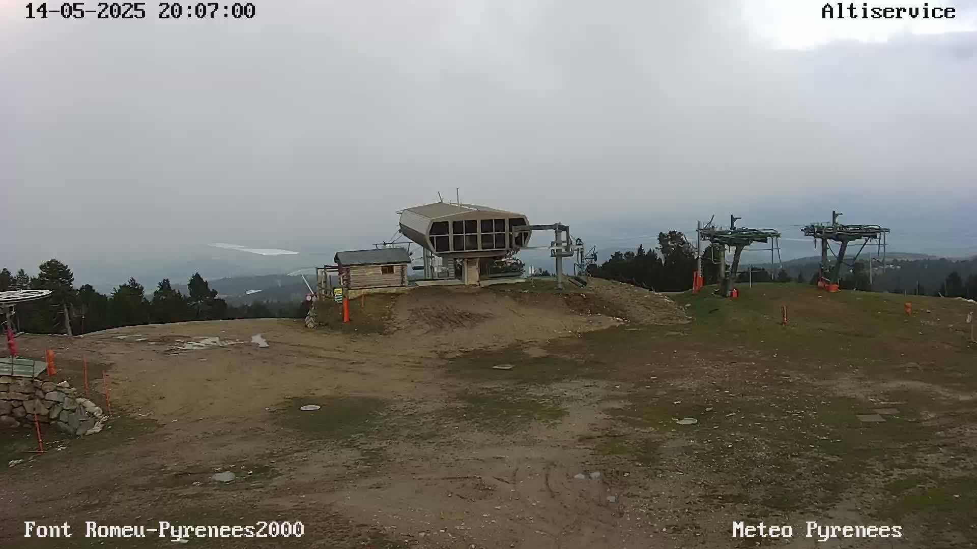 A ski lift station sits atop a barren hill on an overcast day, with distant mountains and a body of water visible in the hazy background.