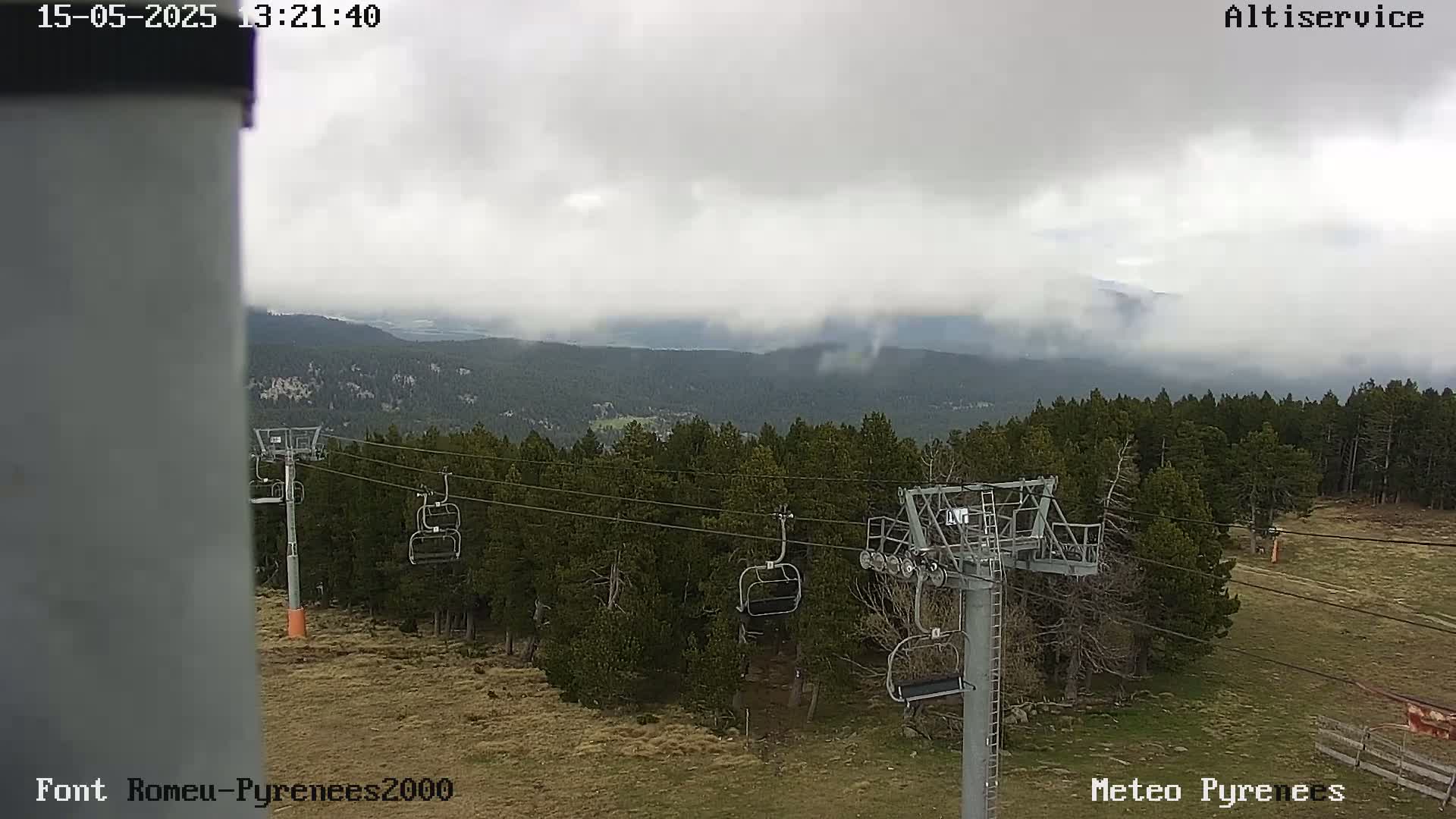 A chairlift stands in a forest overlooking a cloudy mountain range.