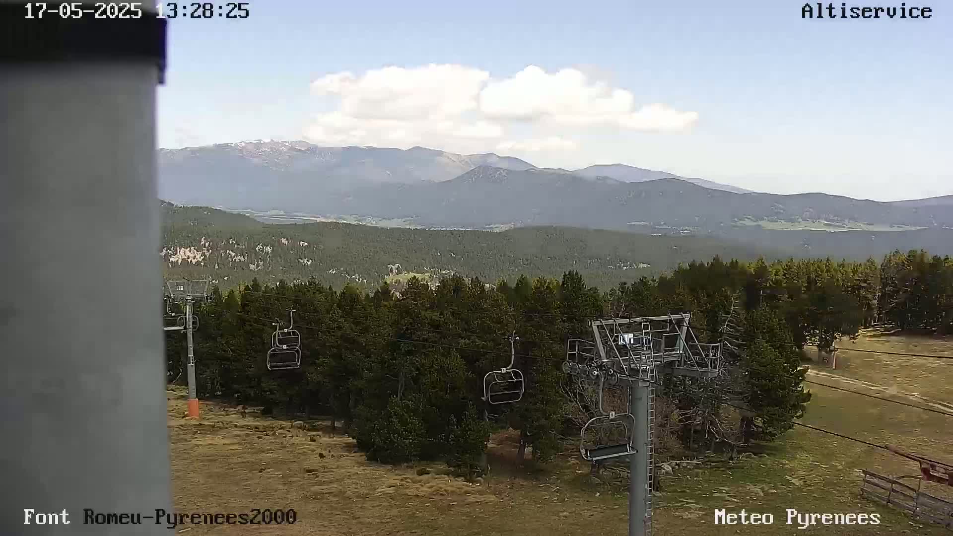 A chairlift sits in a mountainous area with partly cloudy skies and a vast forest.