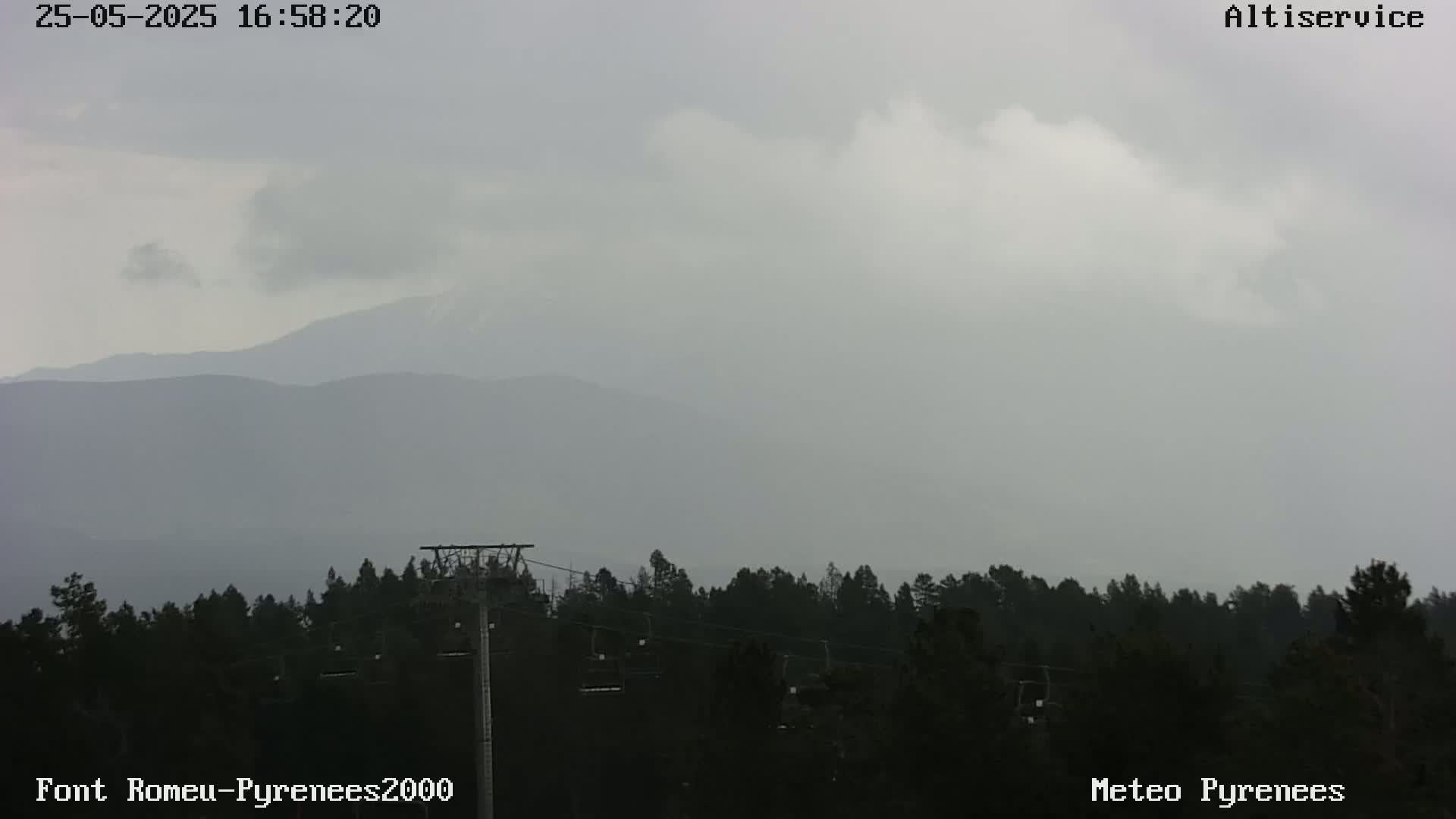 A hazy, overcast sky hangs over a dark forest with a chairlift and distant mountains.