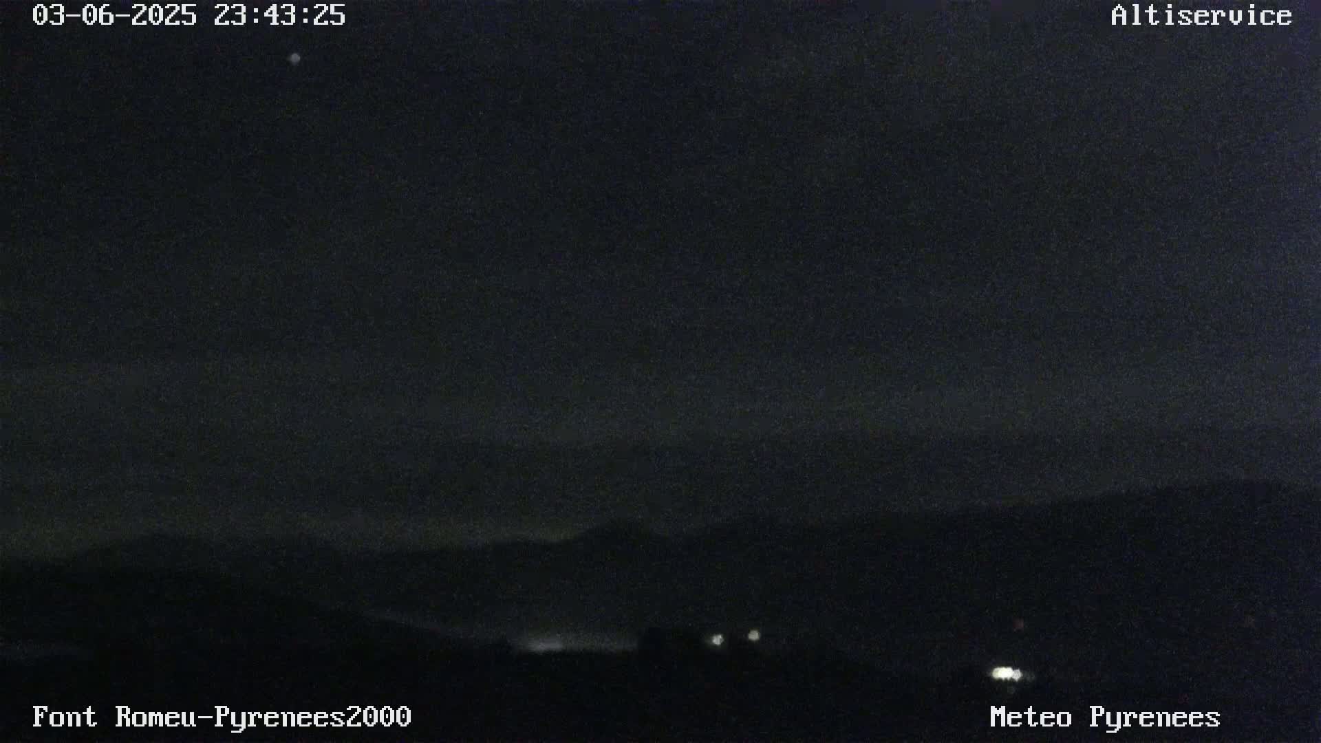 A nighttime, dark view of a mountain range under a mostly clear sky.