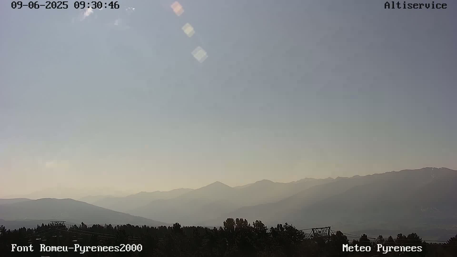 A hazy, pale-blue sky overlooks a range of distant mountains and a foreground of dark, silhouetted trees.