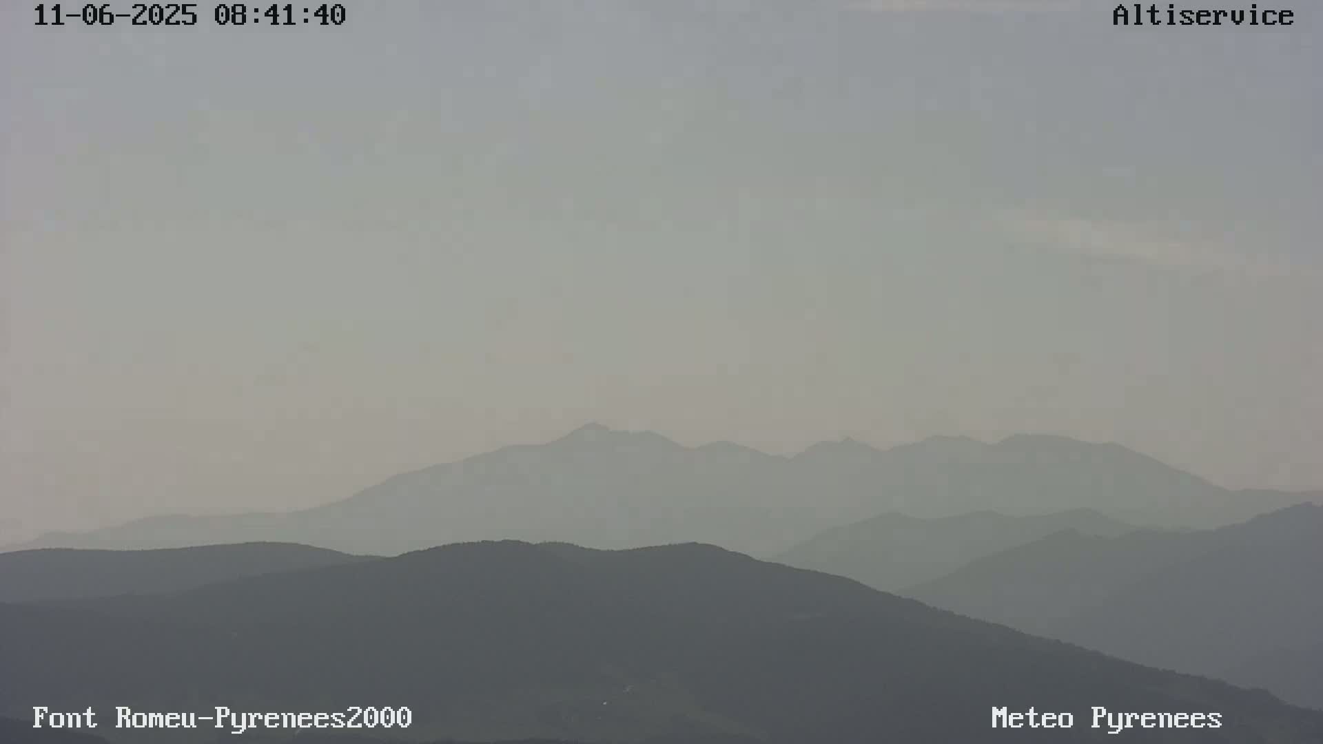 A hazy, light-grey sky overlooks several layers of dark-grey mountains.