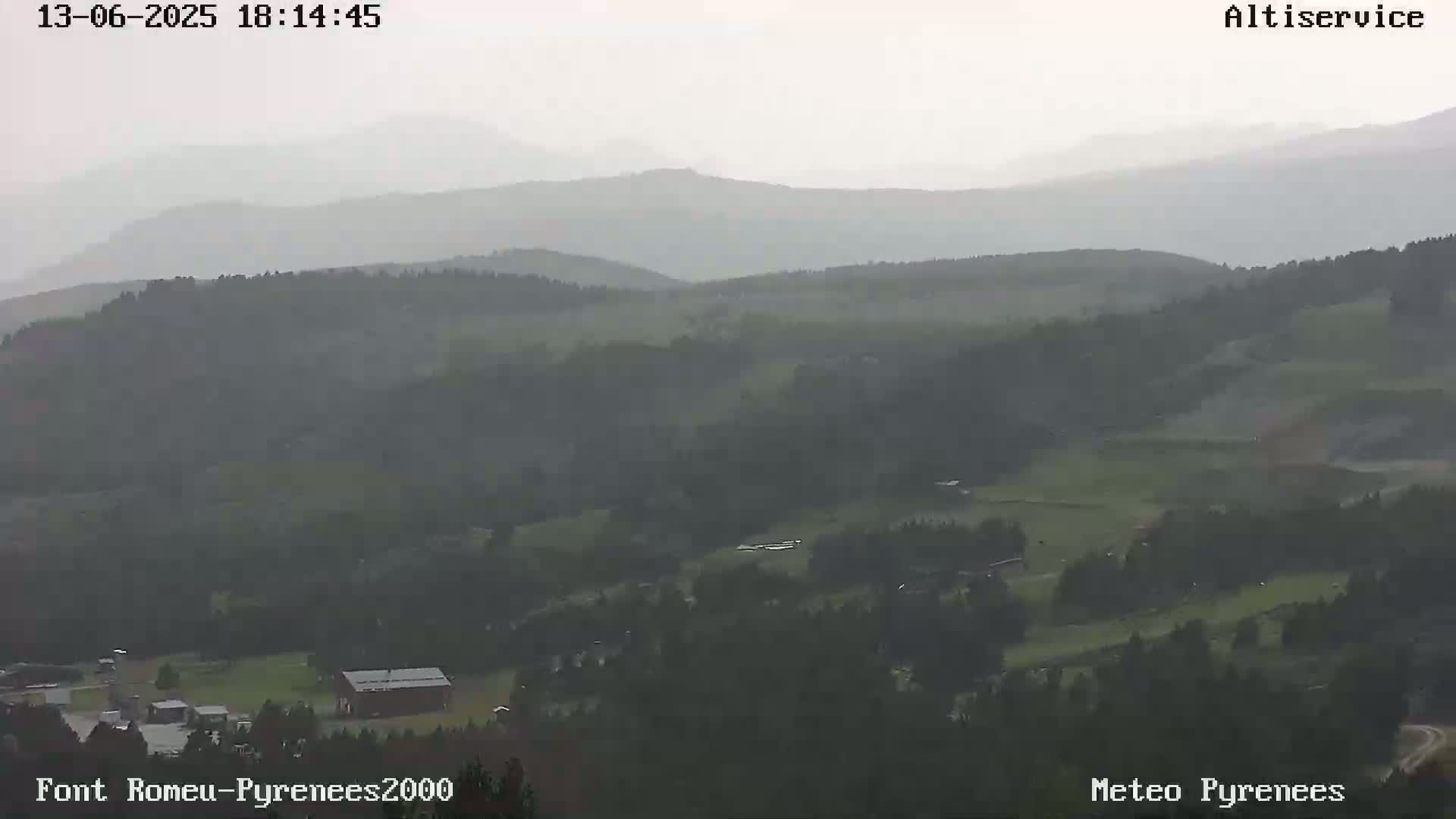 A hazy, overcast view of rolling green hills and distant mountains under a gray sky.