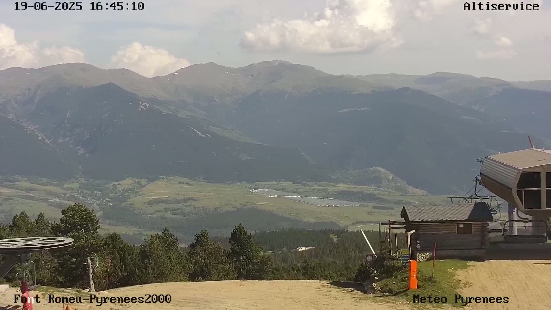 A mountain vista under partly cloudy skies is seen from a ski lift station, with a valley and more mountains in the distance.