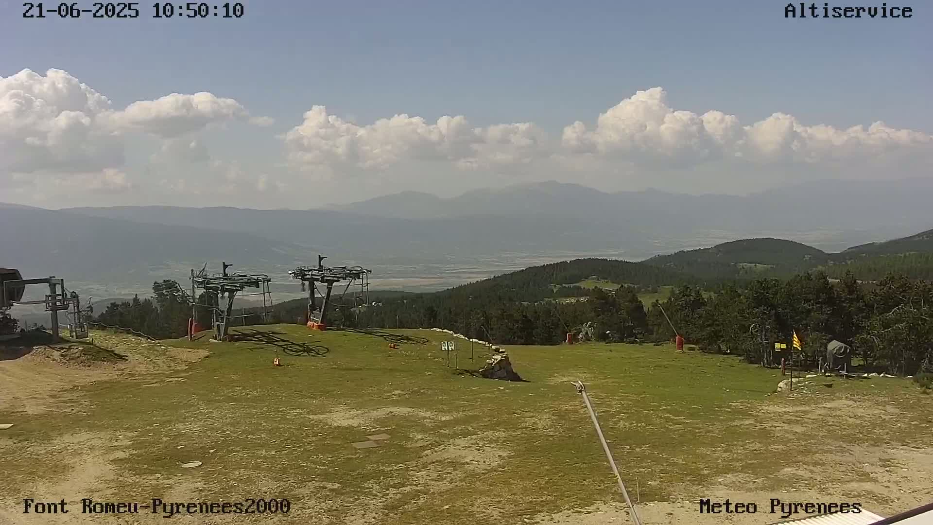 A partly cloudy day reveals a mountain vista overlooking a grassy ski lift area.