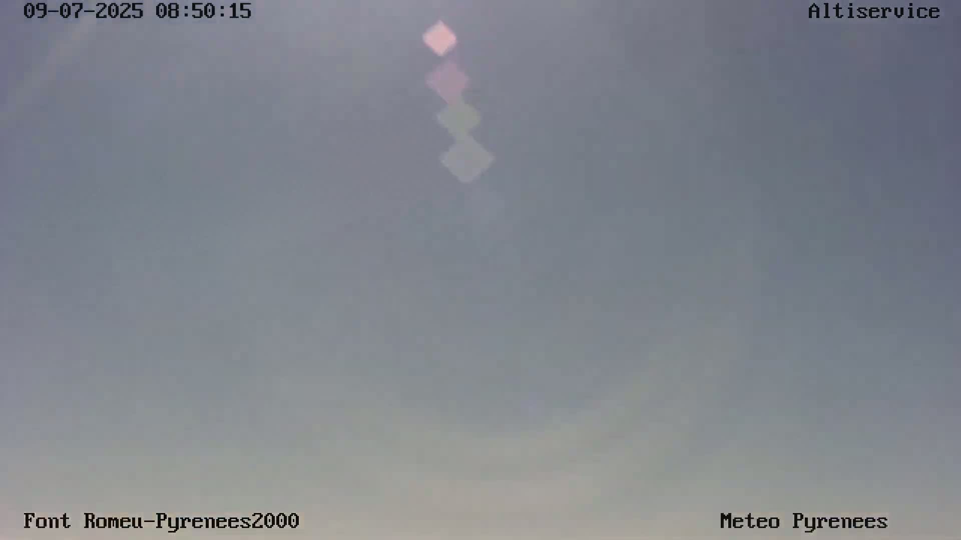 A mostly clear, light-grey sky is visible, with a faint, vertically oriented, multi-colored light source in the center.