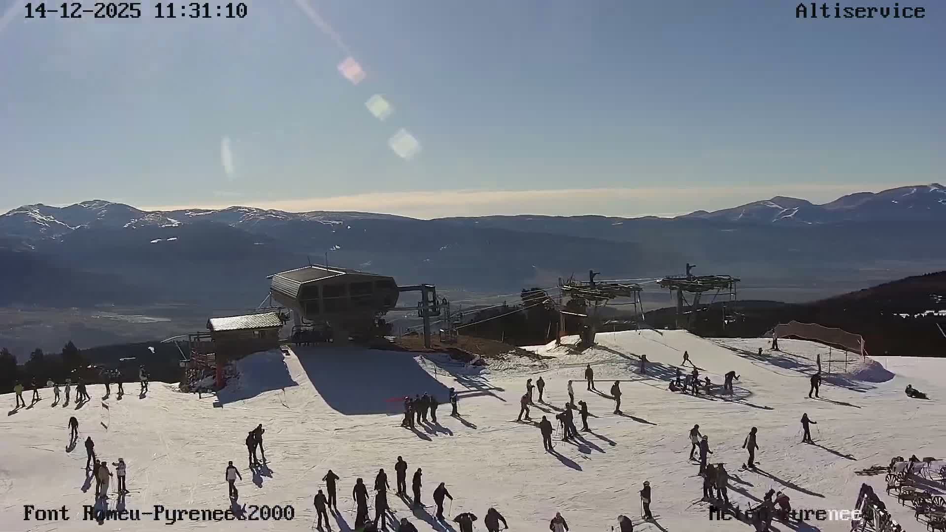 A winter mountain scene shows snow-dusted pine trees and a ski lift in the foreground, with distant peaks largely obscured by heavy fog and an overcast sky.