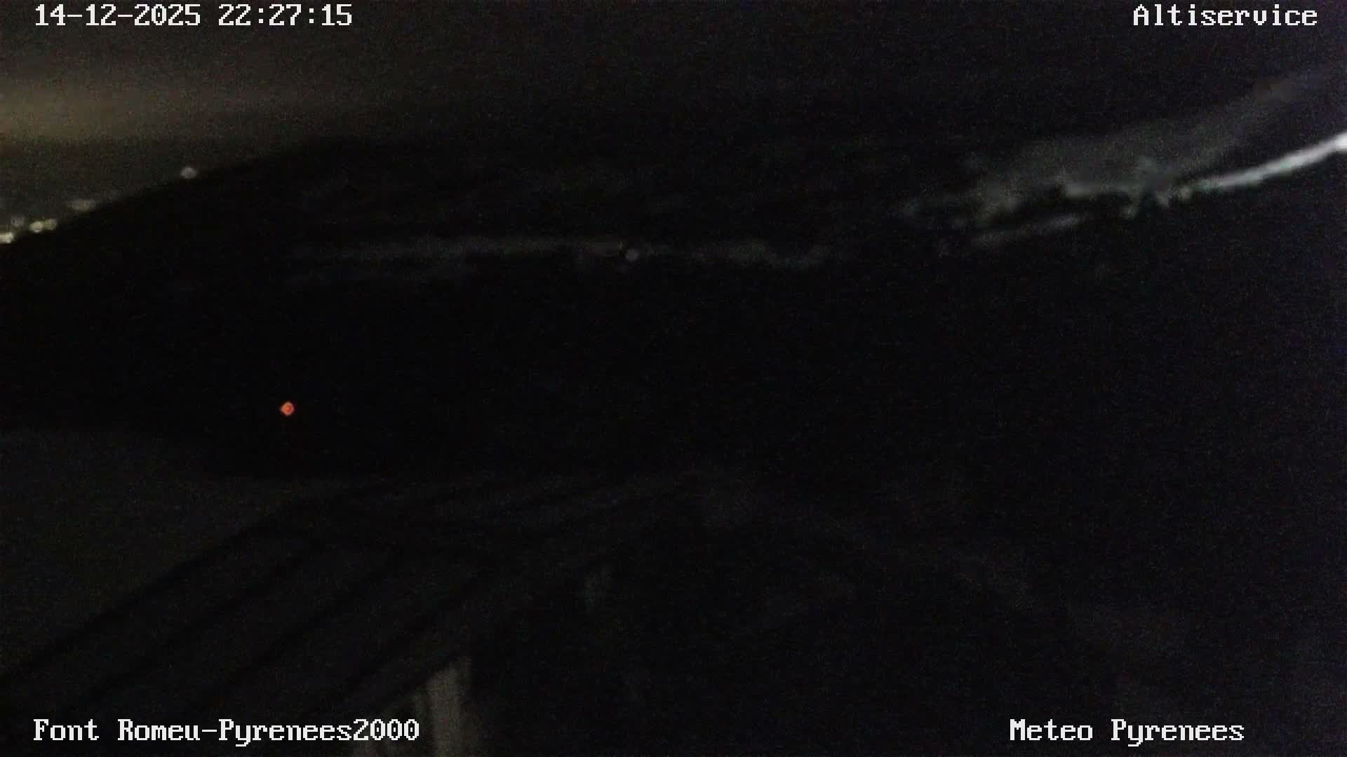 A winter mountain scene shows snow-dusted pine trees and a ski lift in the foreground, with distant peaks largely obscured by heavy fog and an overcast sky.