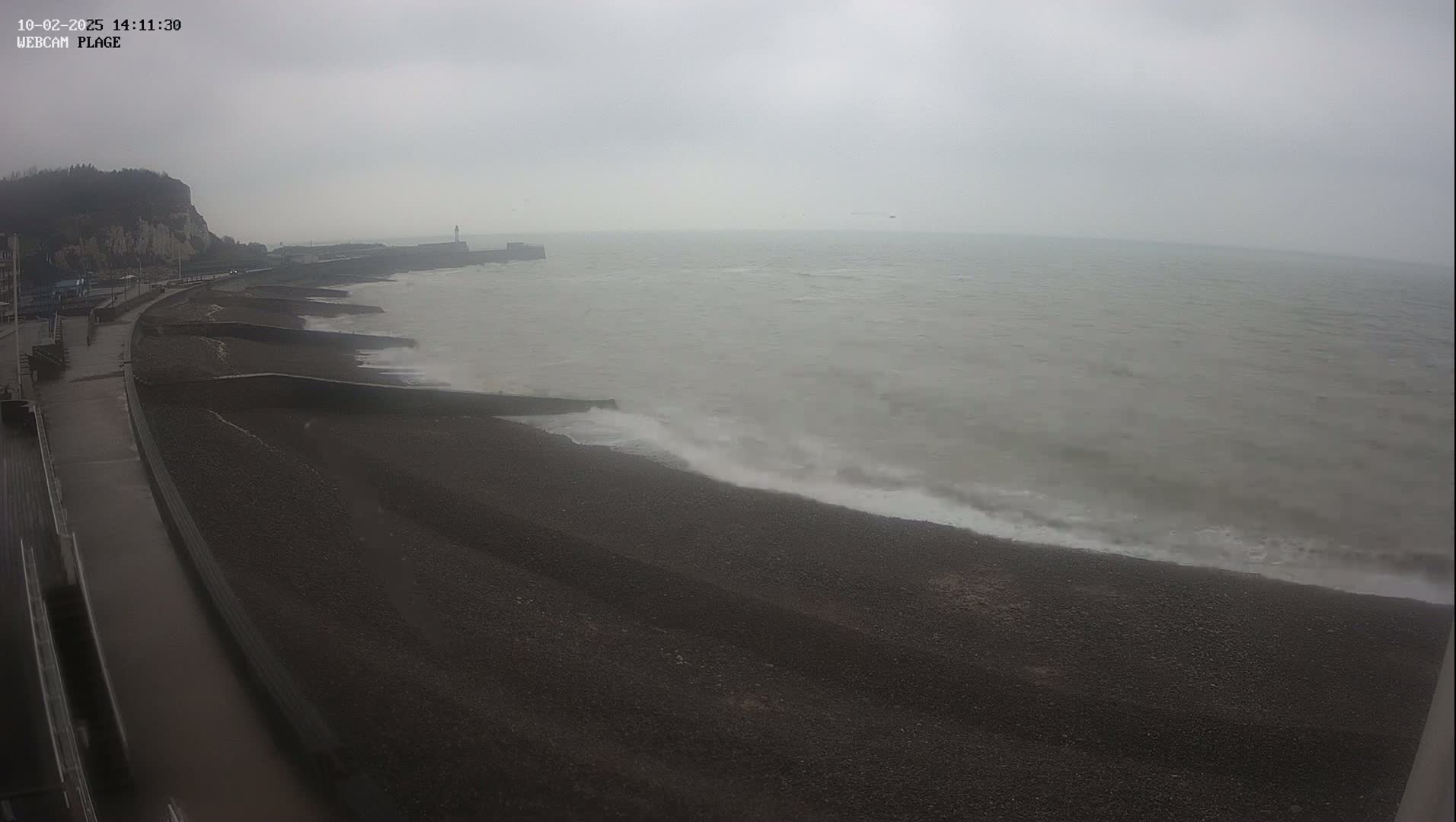 A dark, pebble beach stretches out to a grey, choppy sea under an overcast sky.