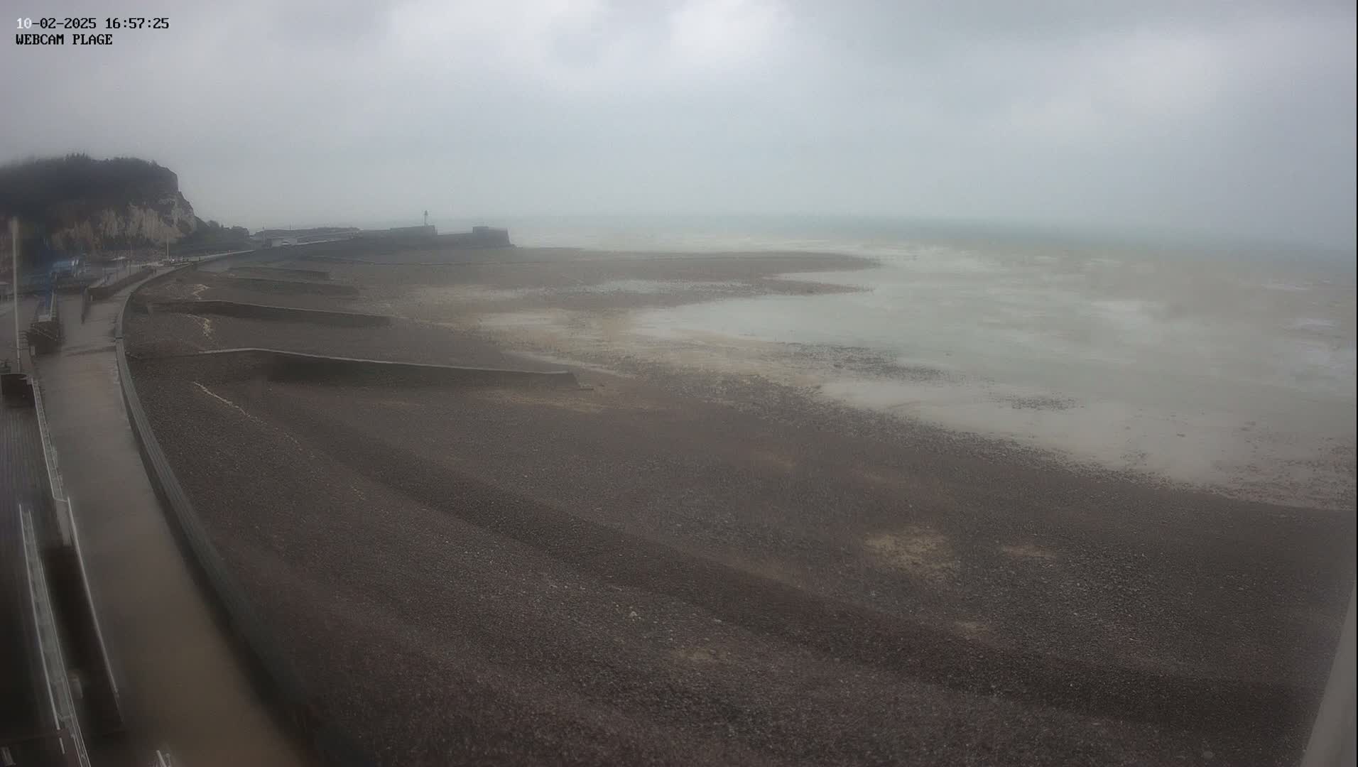 A dark, pebble beach stretches towards a gray, choppy sea under an overcast sky.
