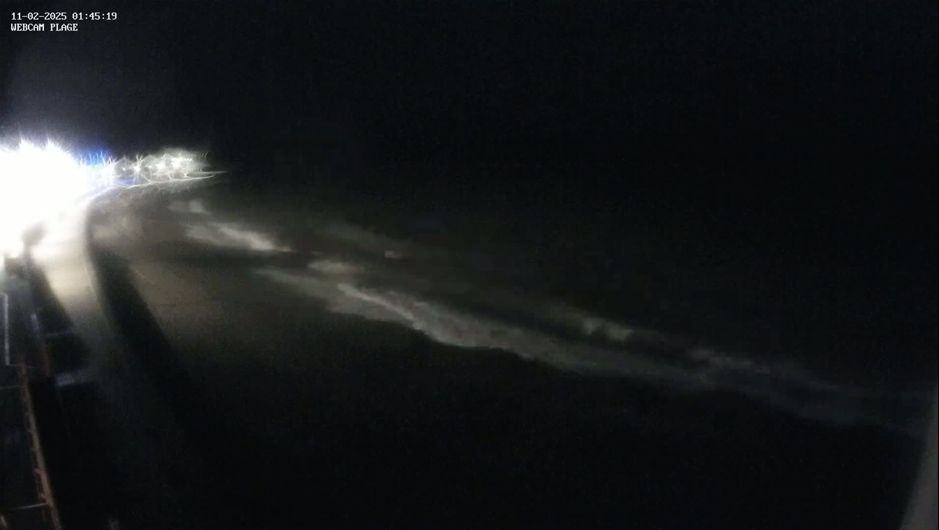 A nighttime, blurry view of a dark, possibly coastal, area with faint, light-colored streaks in the distance, possibly waves or clouds.