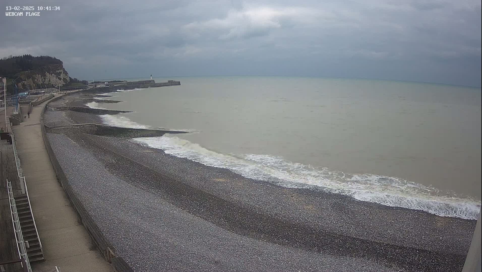 A pebble beach with small waves rolling onto shore under an overcast sky.