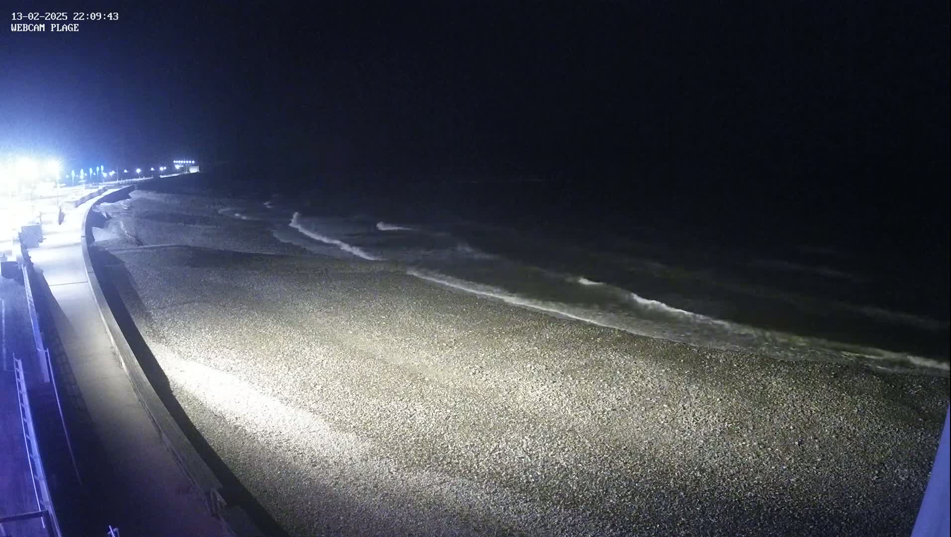 A dark, pebbled beach is gently lapped by waves under a nighttime sky.