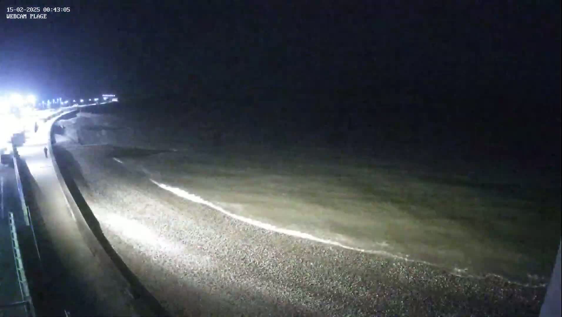 A nighttime view of a pebble beach with gentle waves lapping the shore under a dark sky.