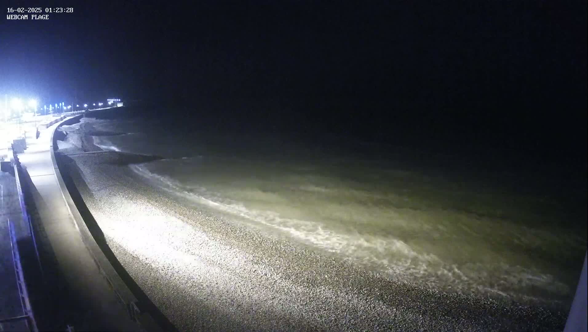 A pebble beach at night is gently lapped by waves under a dark sky.