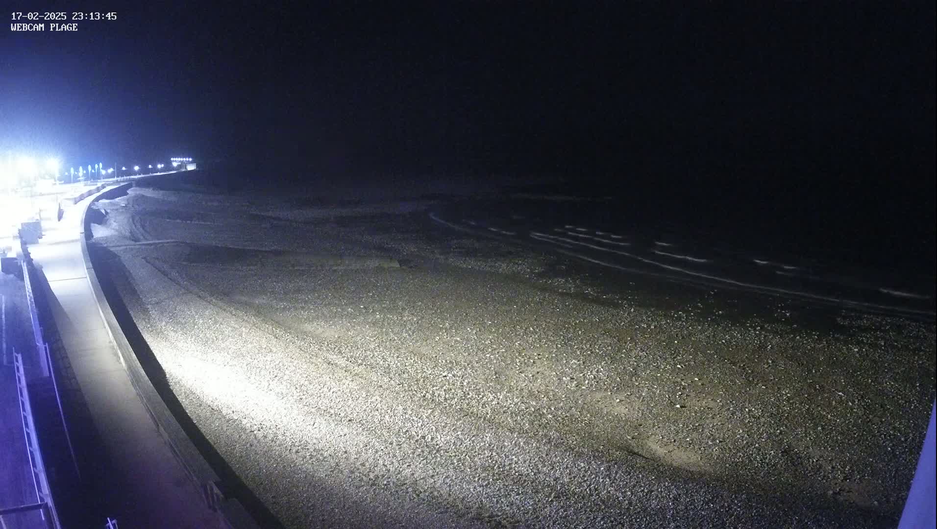 A nighttime view of a pebble beach with gently lapping waves under a dark sky.