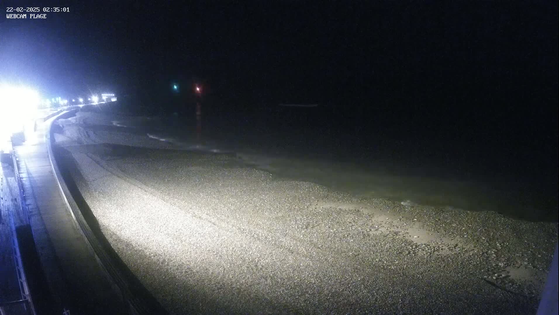 A dark, nighttime view of a pebble beach meeting a calm, dark sea under a clear, starless sky.