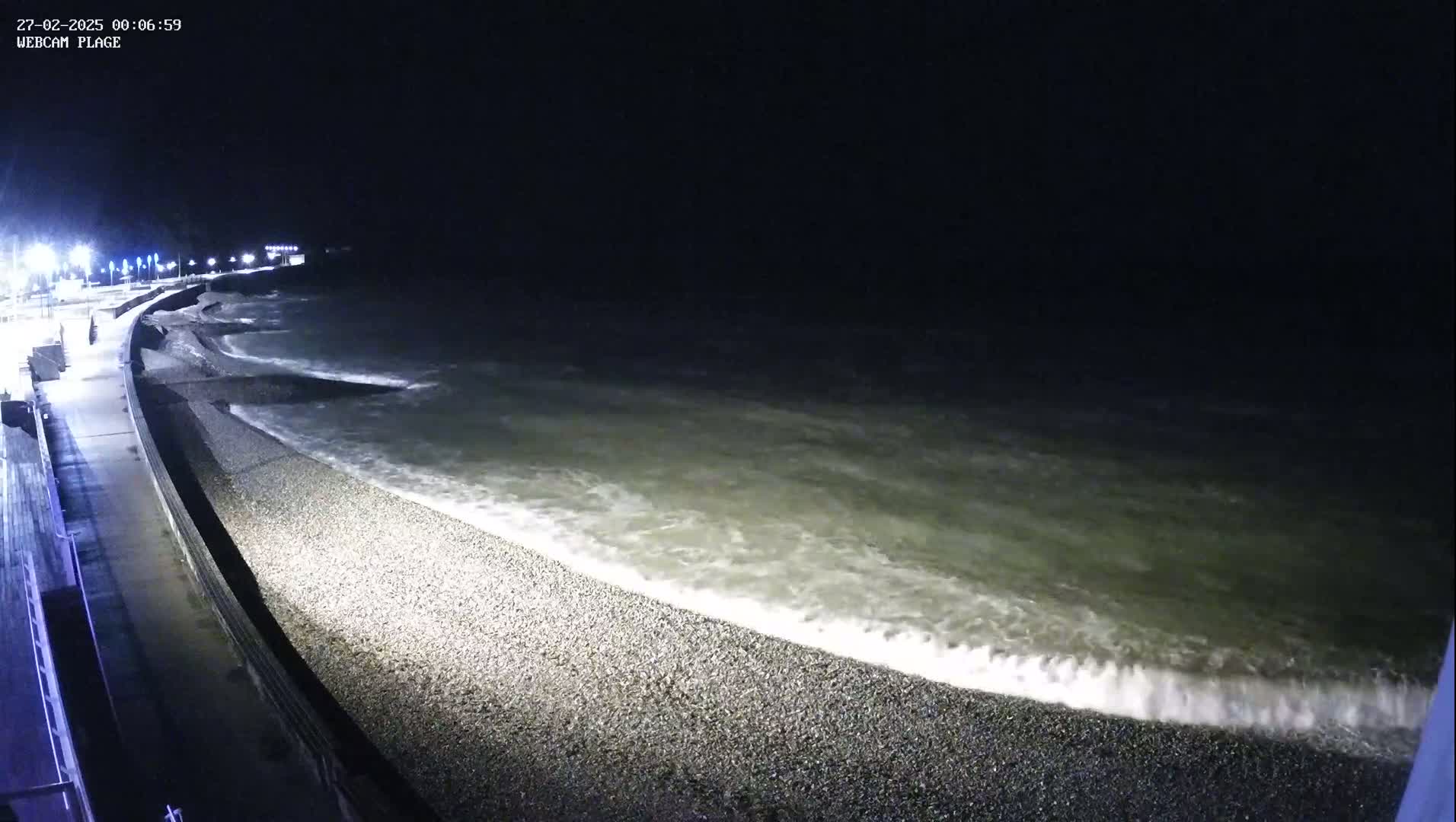 Waves lap a pebble beach at night under a dark sky.