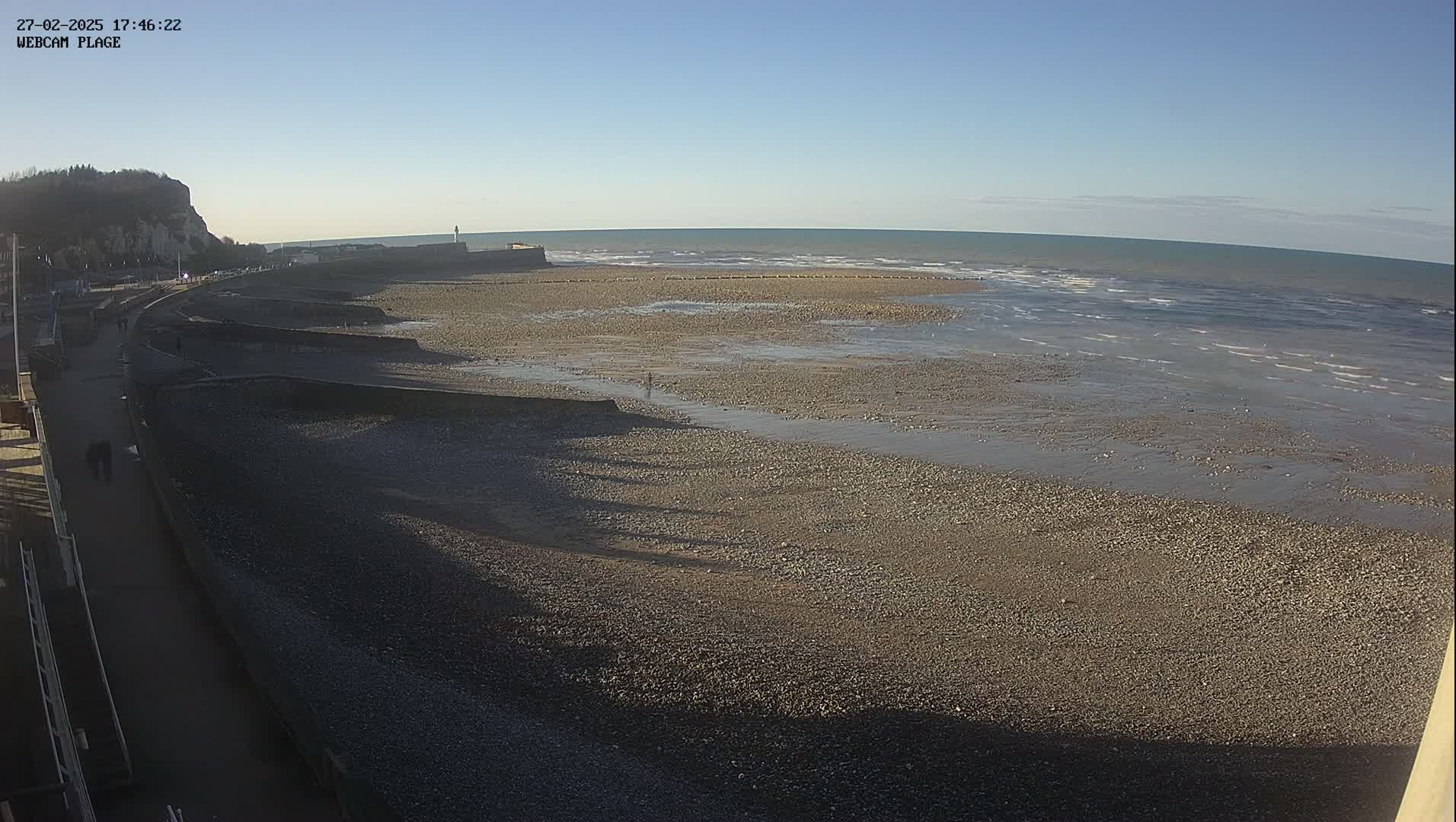 A rocky beach stretches out to a calm sea under a clear blue sky.